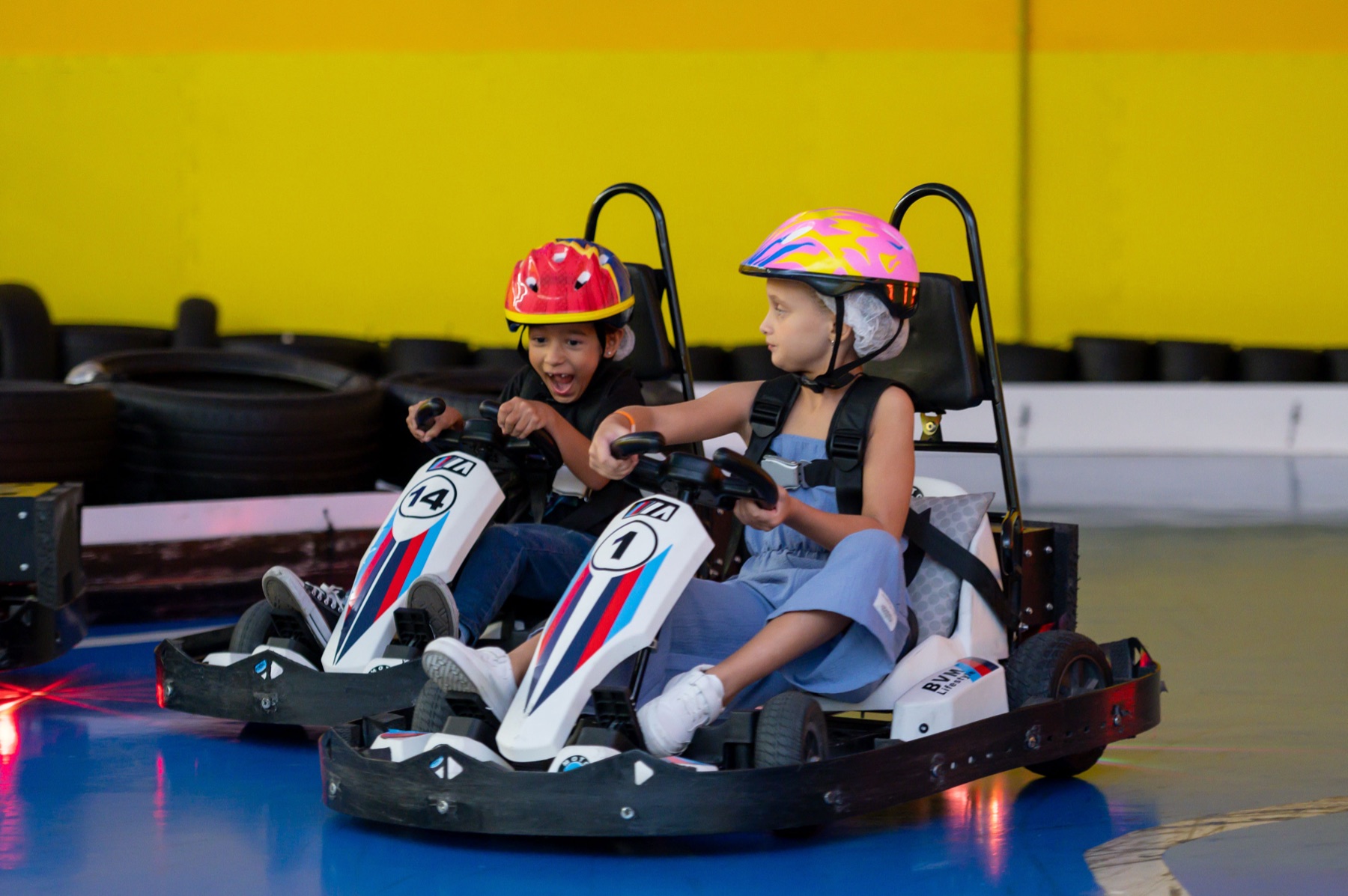 Duas crianças gritando de alegria pilotando karts elétricos na pista